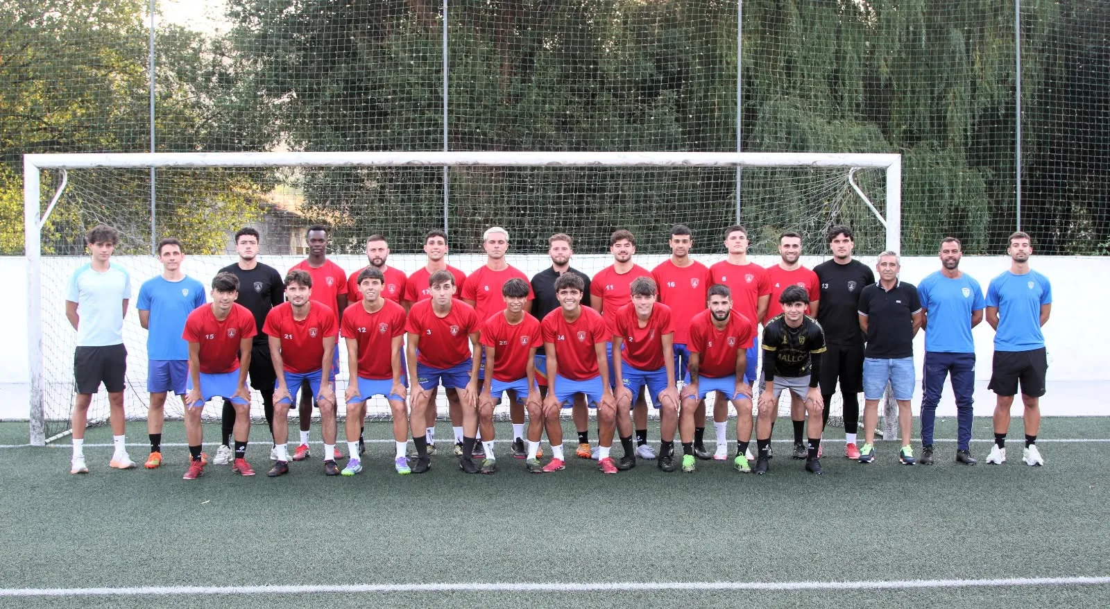 Foto de equipo del Betanzos CF: dos filas de jugadores con camiseta roja y pantalón azul, con el cuerpo técnico a los lados, delante de una portería