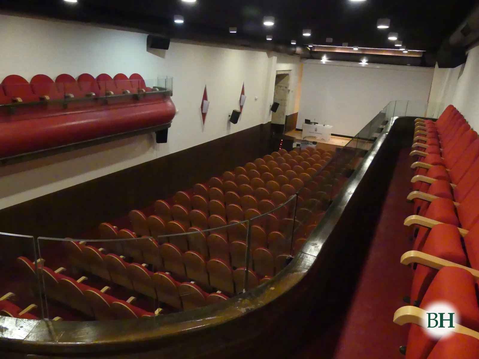 A sala do Teatro Alfonsetti vista desde o anfiteatro: butacas vermellas no patio e nos palcos laterais.