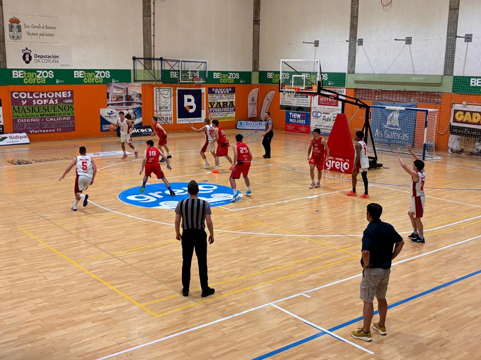 Partido de baloncesto no pavillón municipal de Betanzos: os xogadores do Santo Domingo, de branco e vermello, atacan ante a defensa do Chantada, de vermello e azul.