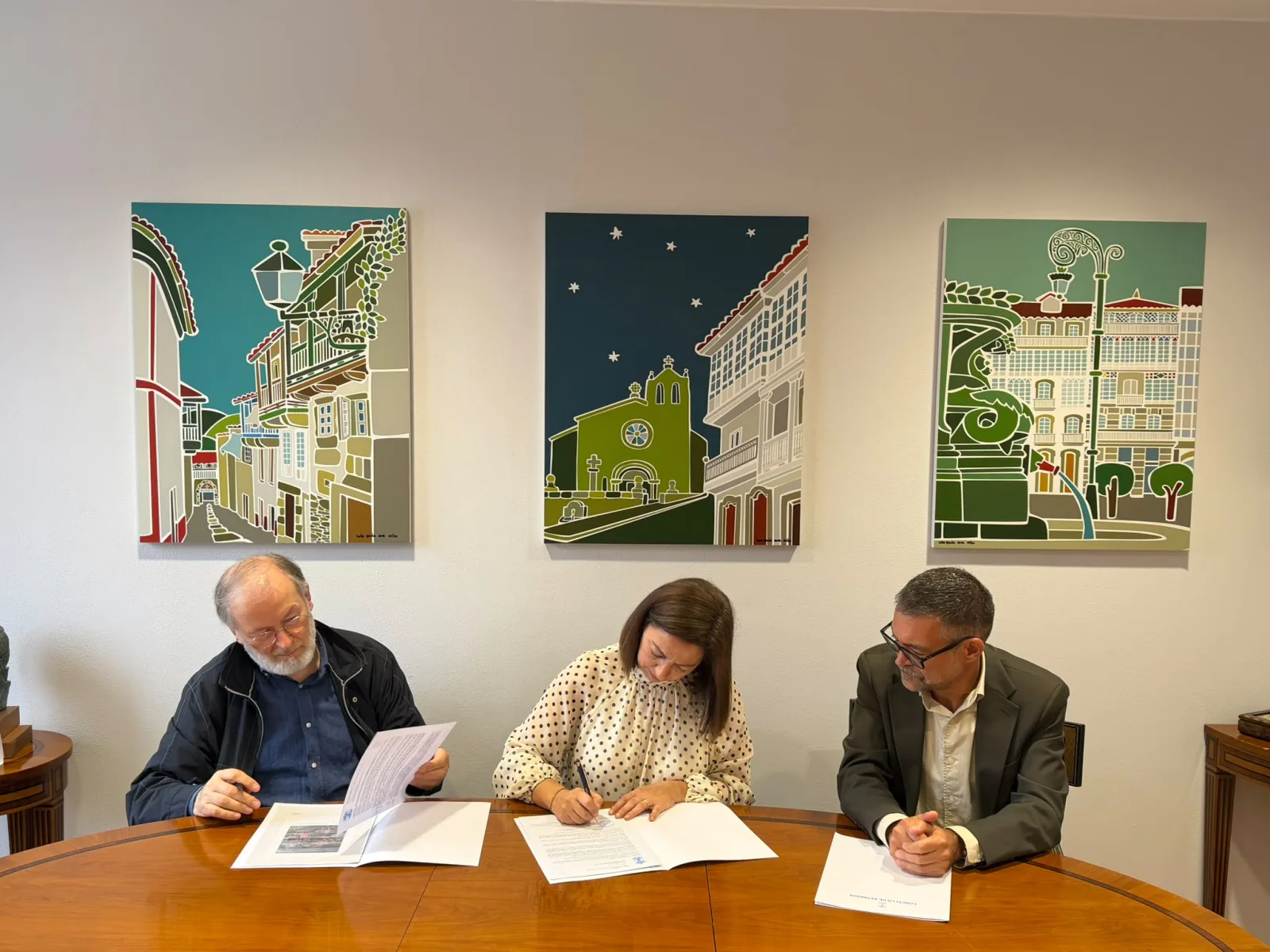 La alcaldesa, María Barral, firma el convenio para restaurar el telón del Alfonsetti junto al presidente de la Fundación L. Monteagudo, Alfredo Erias, que lee el documento, bajo tres cuadros de calles de Betanzos.